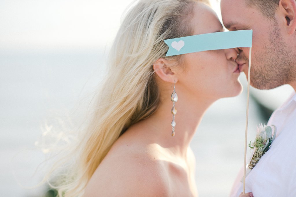 Photo Bride and groom kissing behind a little flag with a heart